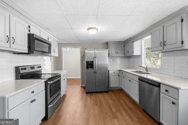 kitchen with gray cabinetry, a sink, wood finished floors, stainless steel appliances, and light countertops