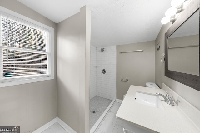 bathroom featuring marble finish floor, a textured ceiling, tiled shower, baseboards, and vanity