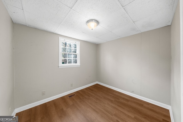 empty room featuring wood finished floors, visible vents, a drop ceiling, and baseboards