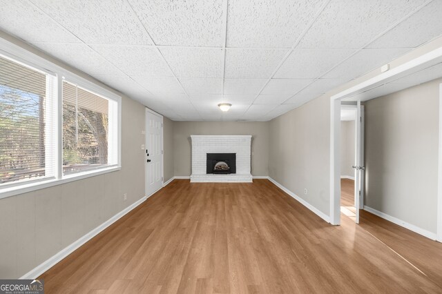 unfurnished living room featuring a brick fireplace, a paneled ceiling, baseboards, and wood finished floors