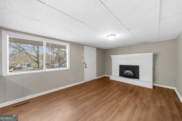 unfurnished living room featuring wood finished floors, visible vents, baseboards, a fireplace, and a paneled ceiling