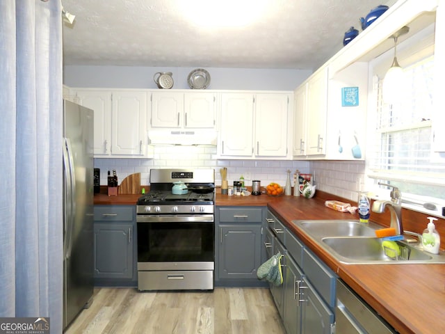 kitchen with a sink, gray cabinetry, white cabinets, appliances with stainless steel finishes, and under cabinet range hood