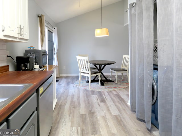 kitchen with pendant lighting, lofted ceiling, light wood-style floors, white cabinetry, and stainless steel dishwasher