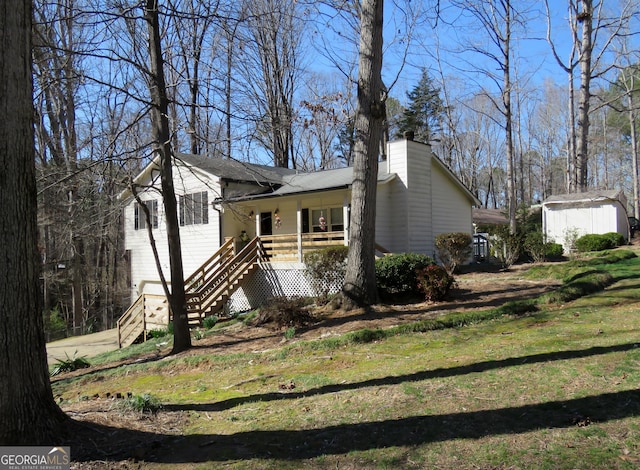 view of front of property with a front yard, an outbuilding, covered porch, a chimney, and stairs