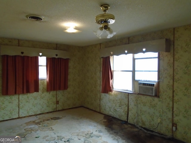 empty room with wallpapered walls, cooling unit, visible vents, and a wealth of natural light