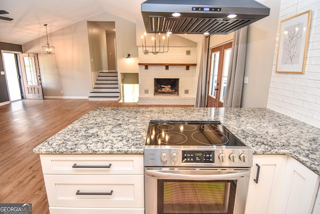 kitchen with light stone counters, lofted ceiling, stainless steel electric stove, under cabinet range hood, and open floor plan