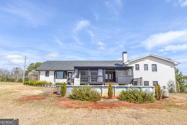 rear view of house featuring roof with shingles, a sunroom, an outdoor pool, brick siding, and a chimney