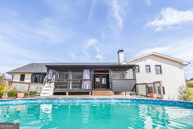 rear view of property with an outdoor pool, brick siding, a chimney, and a sunroom