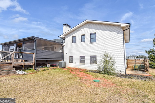 rear view of property featuring central AC, a yard, a sunroom, brick siding, and a chimney