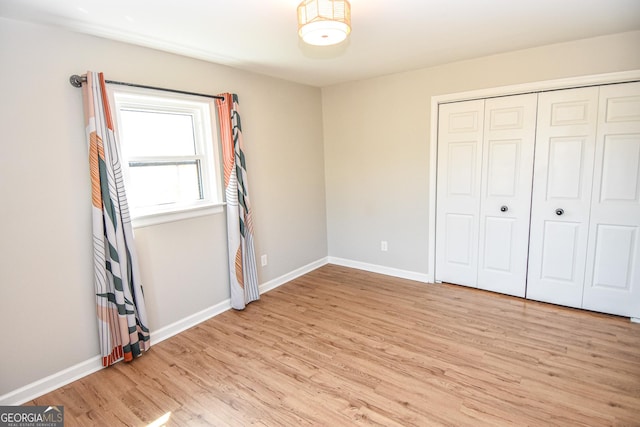 unfurnished bedroom with a closet, baseboards, and light wood finished floors