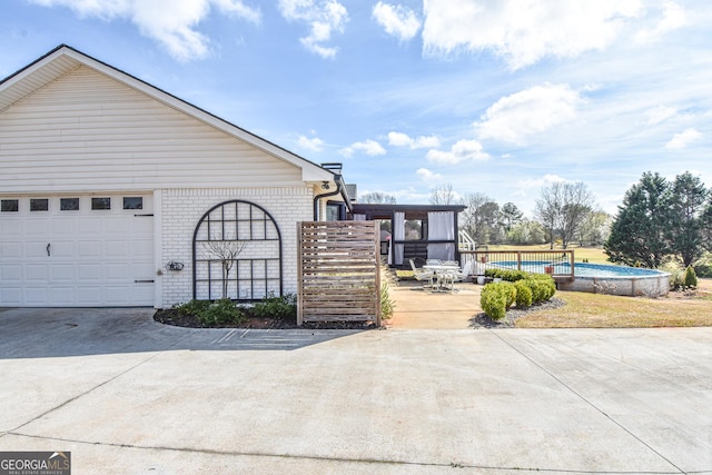 exterior space featuring brick siding, an outdoor pool, concrete driveway, and a garage