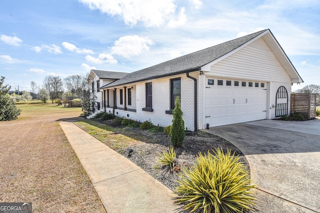 view of side of property featuring brick siding, driveway, an attached garage, and roof with shingles