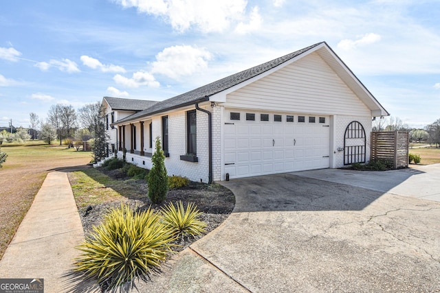 view of side of home featuring concrete driveway, an attached garage, brick siding, and a shingled roof