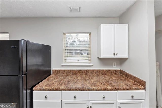 kitchen with dark countertops, visible vents, freestanding refrigerator, white cabinets, and a textured ceiling