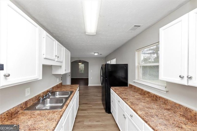 kitchen featuring light wood-style flooring, freestanding refrigerator, white cabinets, a textured ceiling, and a sink