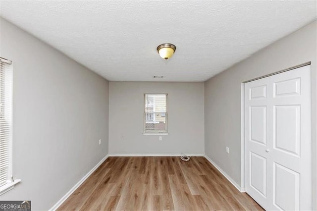 unfurnished bedroom featuring a textured ceiling, light wood-type flooring, and baseboards