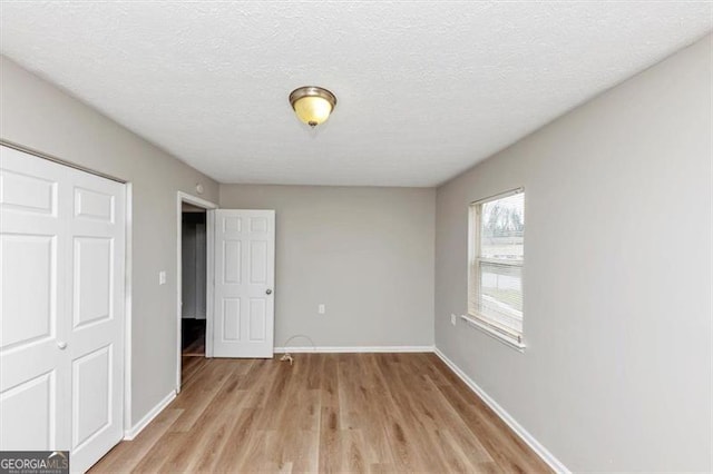 unfurnished bedroom with a closet, baseboards, a textured ceiling, and light wood finished floors