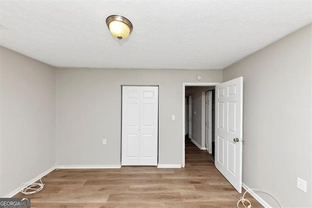 unfurnished bedroom with a closet, a textured ceiling, light wood-type flooring, and baseboards