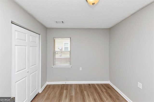 unfurnished bedroom with light wood finished floors, visible vents, a textured ceiling, and baseboards