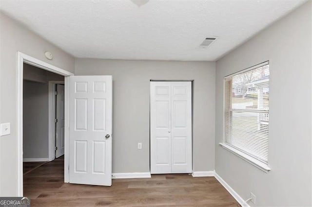 unfurnished bedroom with a textured ceiling, wood finished floors, visible vents, and baseboards