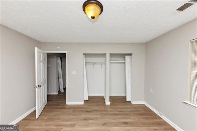 unfurnished bedroom with visible vents, a textured ceiling, baseboards, and light wood-style floors