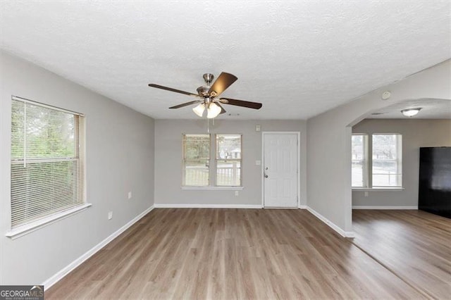 unfurnished living room featuring arched walkways, a ceiling fan, baseboards, and wood finished floors