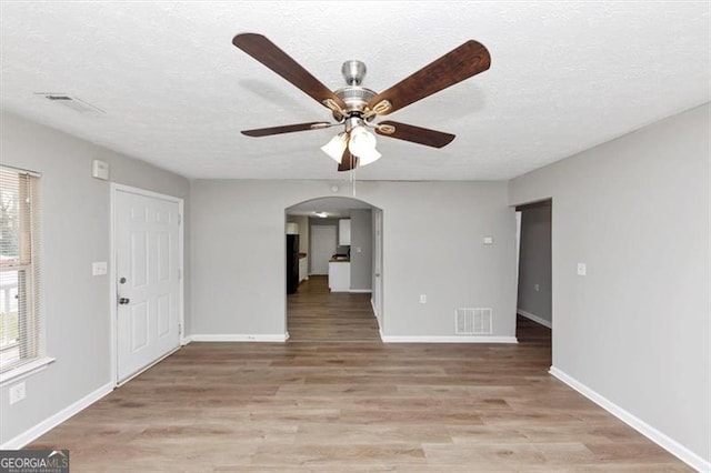 unfurnished living room with visible vents, arched walkways, ceiling fan, a textured ceiling, and light wood-type flooring