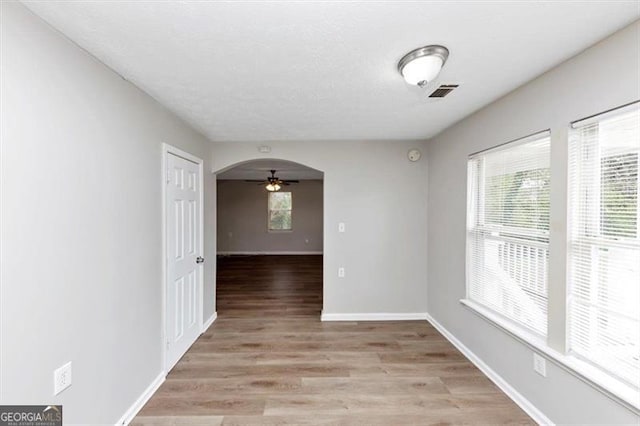 empty room with visible vents, a healthy amount of sunlight, a ceiling fan, and light wood finished floors