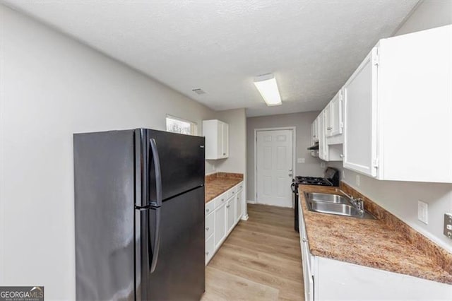 kitchen with gas stove, freestanding refrigerator, a sink, white cabinets, and light wood-type flooring