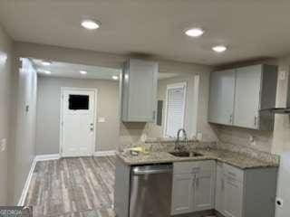 kitchen with a sink, stainless steel dishwasher, wood finished floors, and light countertops