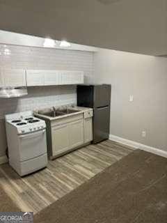 kitchen featuring light wood-type flooring, white gas stove, a sink, freestanding refrigerator, and baseboards