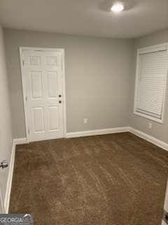 spare room featuring baseboards and dark carpet