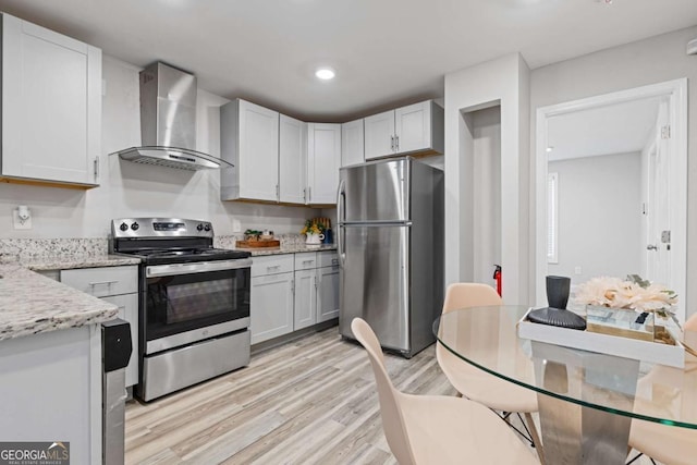 kitchen with recessed lighting, light wood-style floors, appliances with stainless steel finishes, wall chimney range hood, and light stone countertops