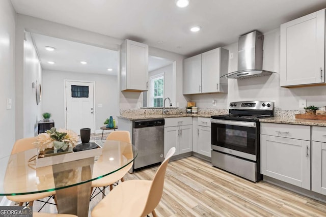 kitchen featuring light wood-type flooring, recessed lighting, stainless steel appliances, wall chimney range hood, and light stone countertops