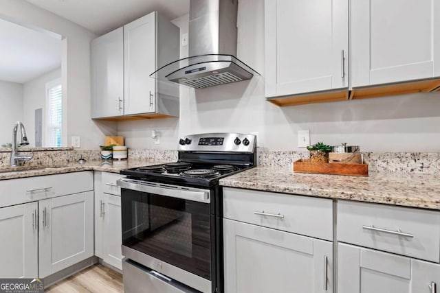 kitchen with wall chimney range hood, light stone countertops, light wood-style flooring, stainless steel range with electric cooktop, and a sink