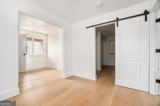 spare room with a barn door, baseboards, visible vents, and light wood finished floors