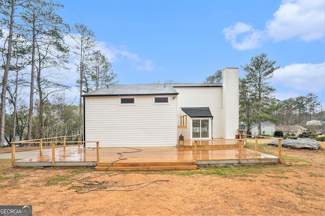 back of house featuring a wooden deck, a chimney, and a shingled roof