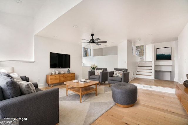 living room featuring wood finished floors, baseboards, visible vents, a ceiling fan, and stairs