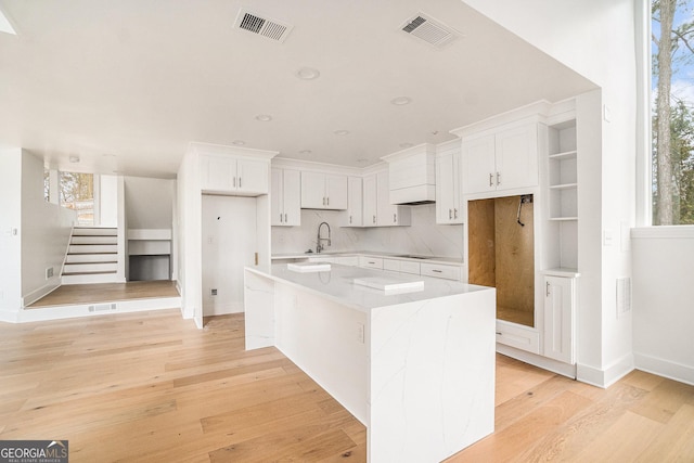 kitchen with visible vents, white cabinets, light wood-style flooring, and a sink