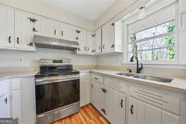 kitchen with under cabinet range hood, stainless steel electric range oven, light countertops, white cabinets, and a sink