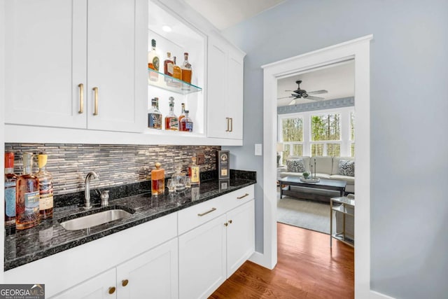 bar featuring a sink, backsplash, dark wood finished floors, wet bar, and ceiling fan