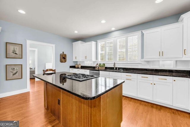 kitchen featuring a sink, a kitchen island, dark stone counters, white cabinets, and light wood finished floors