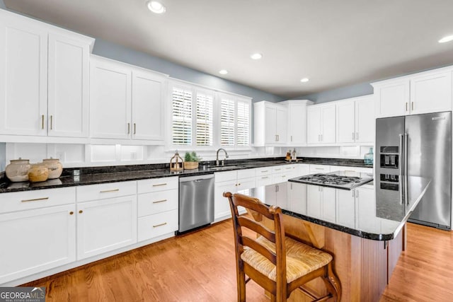 kitchen with light wood finished floors, white cabinets, appliances with stainless steel finishes, and a breakfast bar