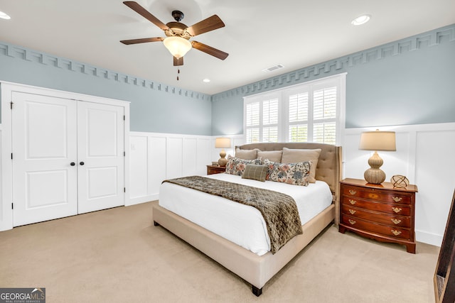 bedroom with a ceiling fan, a wainscoted wall, visible vents, multiple closets, and light carpet