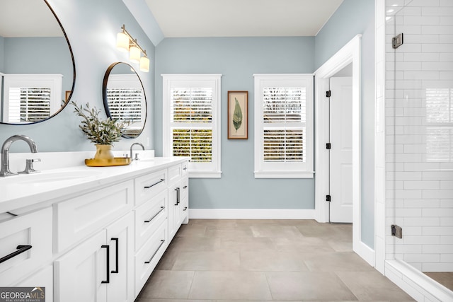 full bath featuring double vanity, a stall shower, baseboards, and a sink