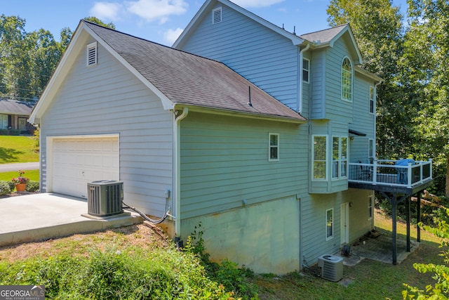 view of side of property featuring a garage, cooling unit, driveway, and roof with shingles