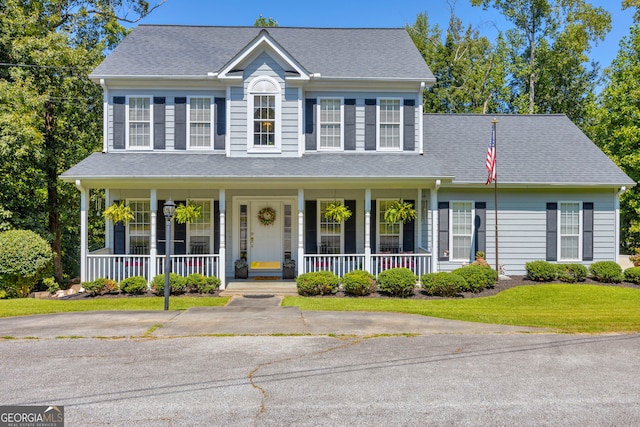 view of front of property with roof with shingles, covered porch, and a front lawn