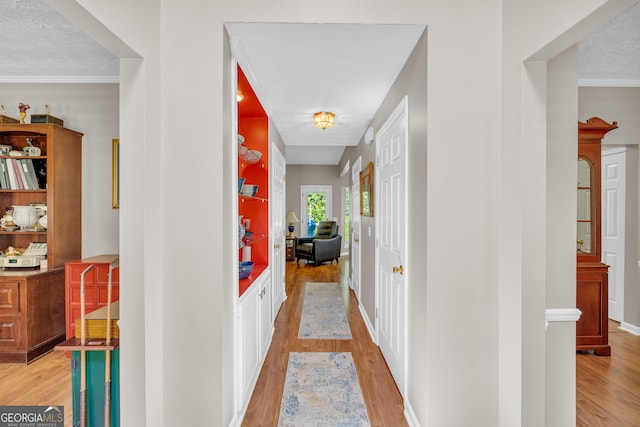 hall with light wood-style floors, ornamental molding, and a textured ceiling