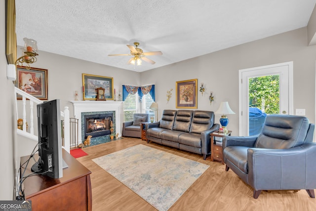 living area featuring a textured ceiling, a glass covered fireplace, a ceiling fan, and light wood finished floors