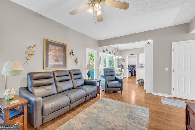 living area featuring light wood-style flooring, ceiling fan with notable chandelier, baseboards, and a textured ceiling